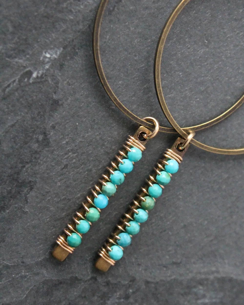 Close up of the Wild Balance Telluride Earrings in Turquoise resting on a stone background