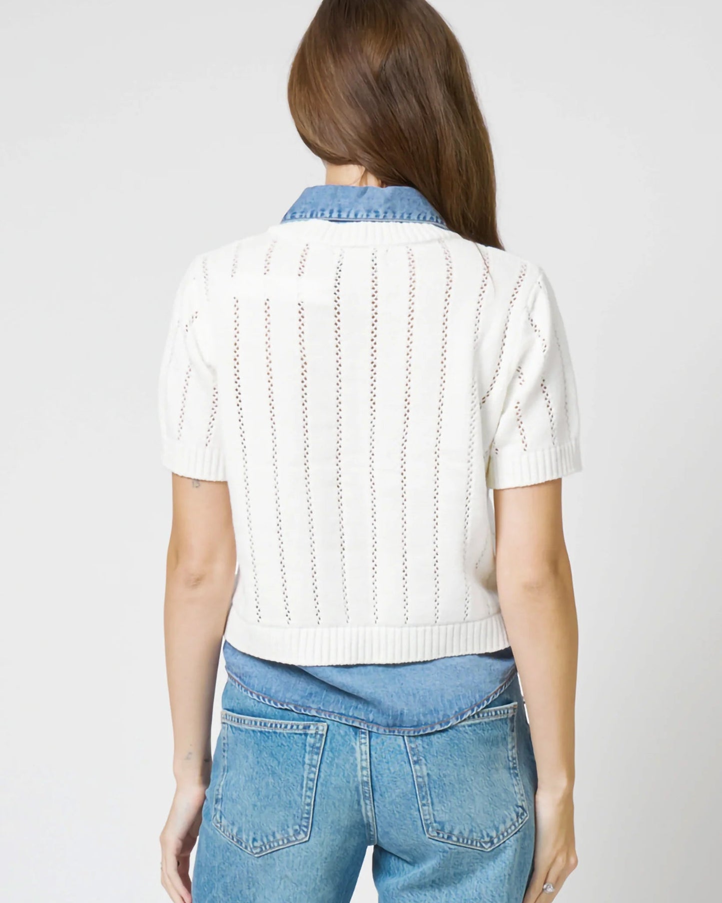 Woman wearing a white knit top and blue jeans on a plain background