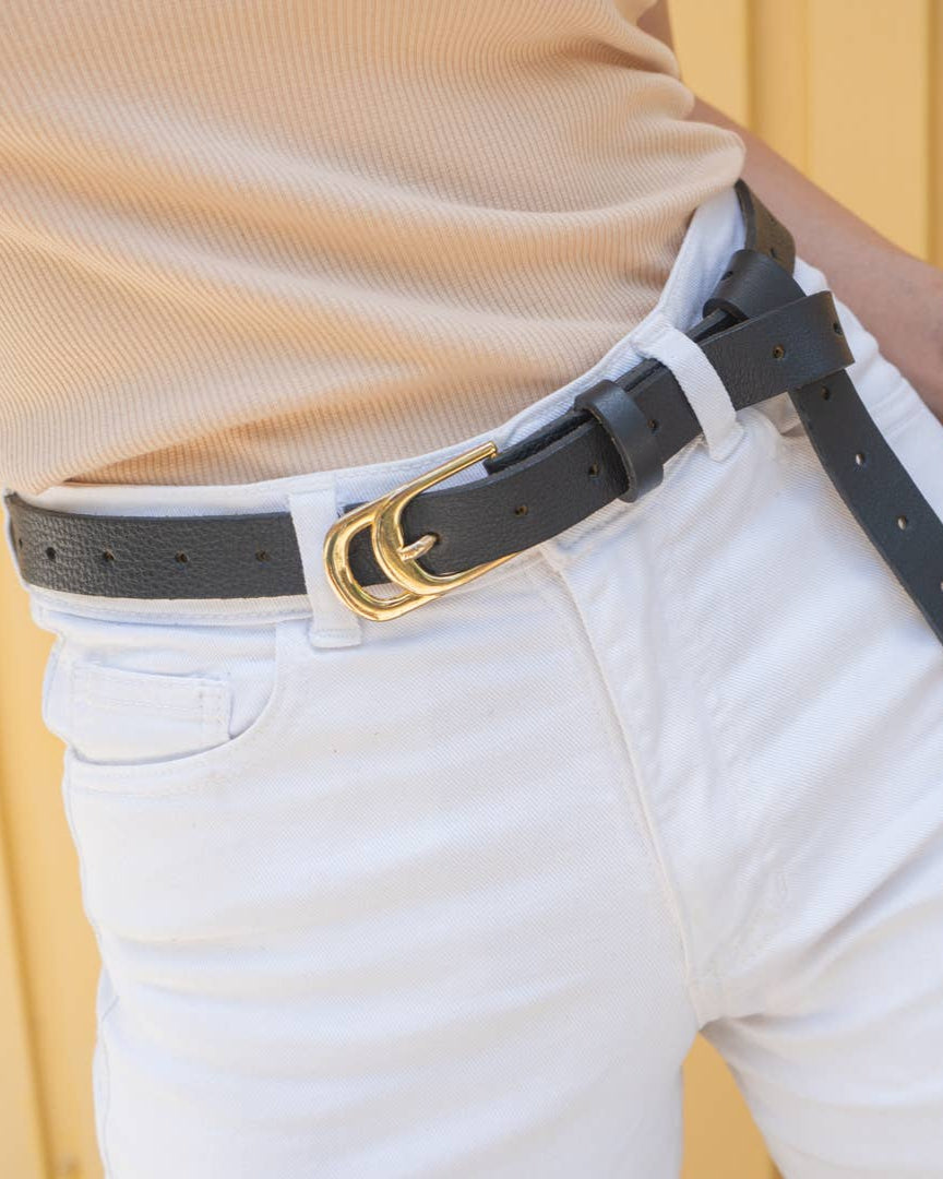 Person wearing a black belt with a gold buckle on white pants against a yellow background