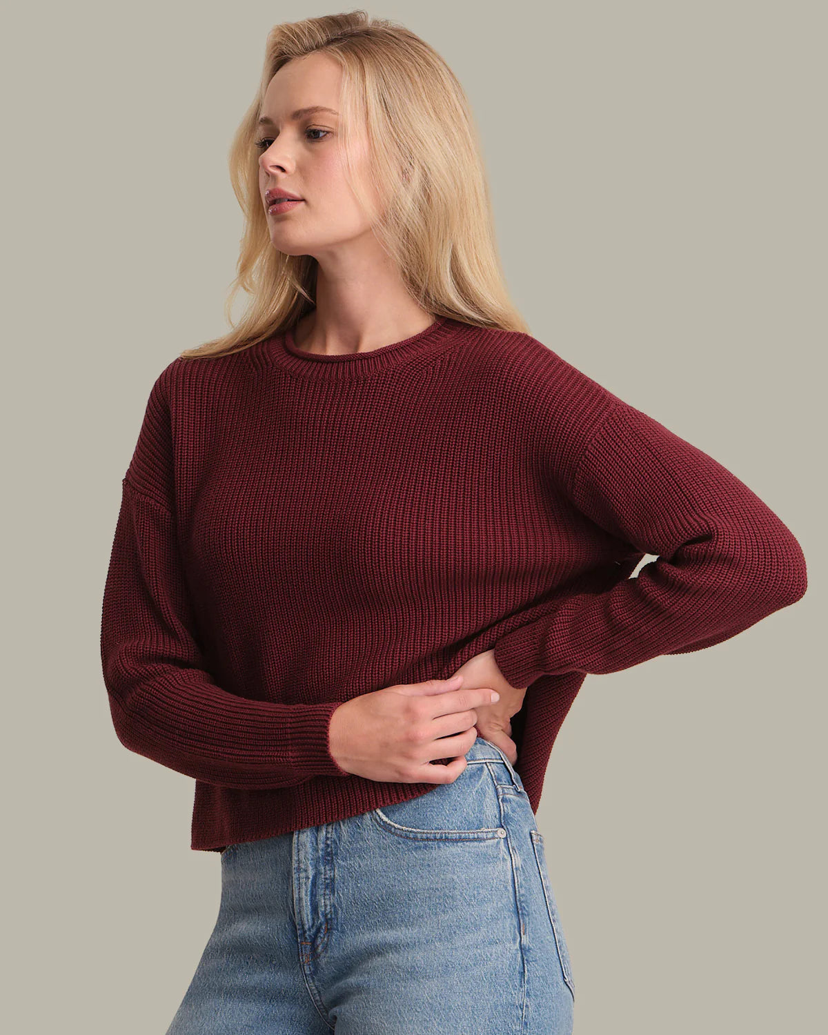 Woman wearing a burgundy sweater and blue jeans against a plain background
