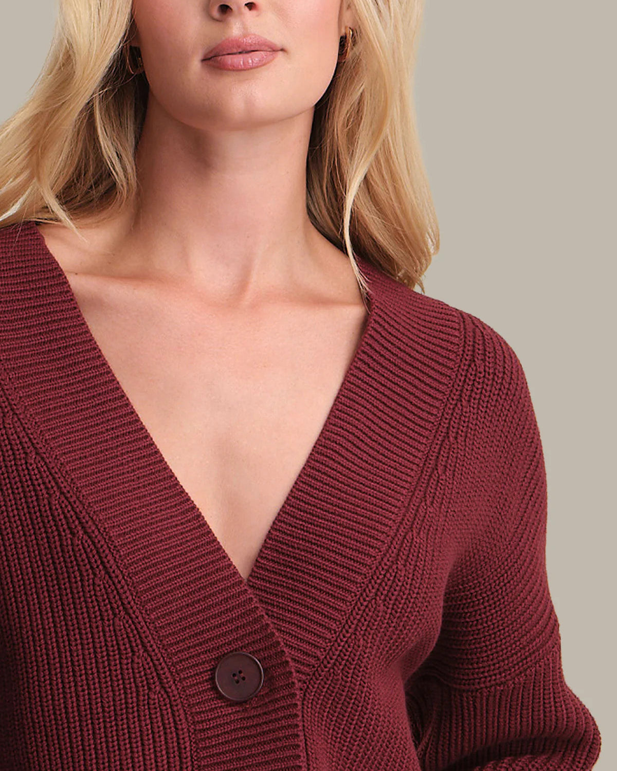 Close-up of a person wearing a burgundy knitted cardigan on a neutral background