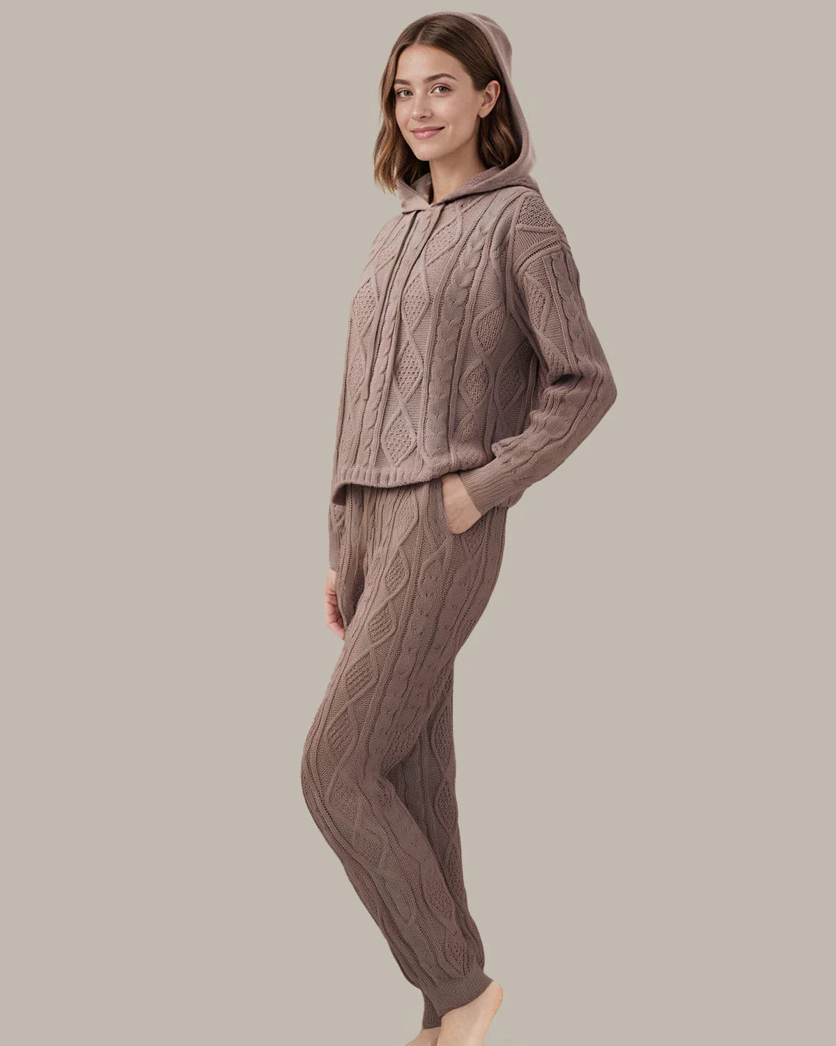Woman wearing a cable knit hoodie and pants set on a neutral background