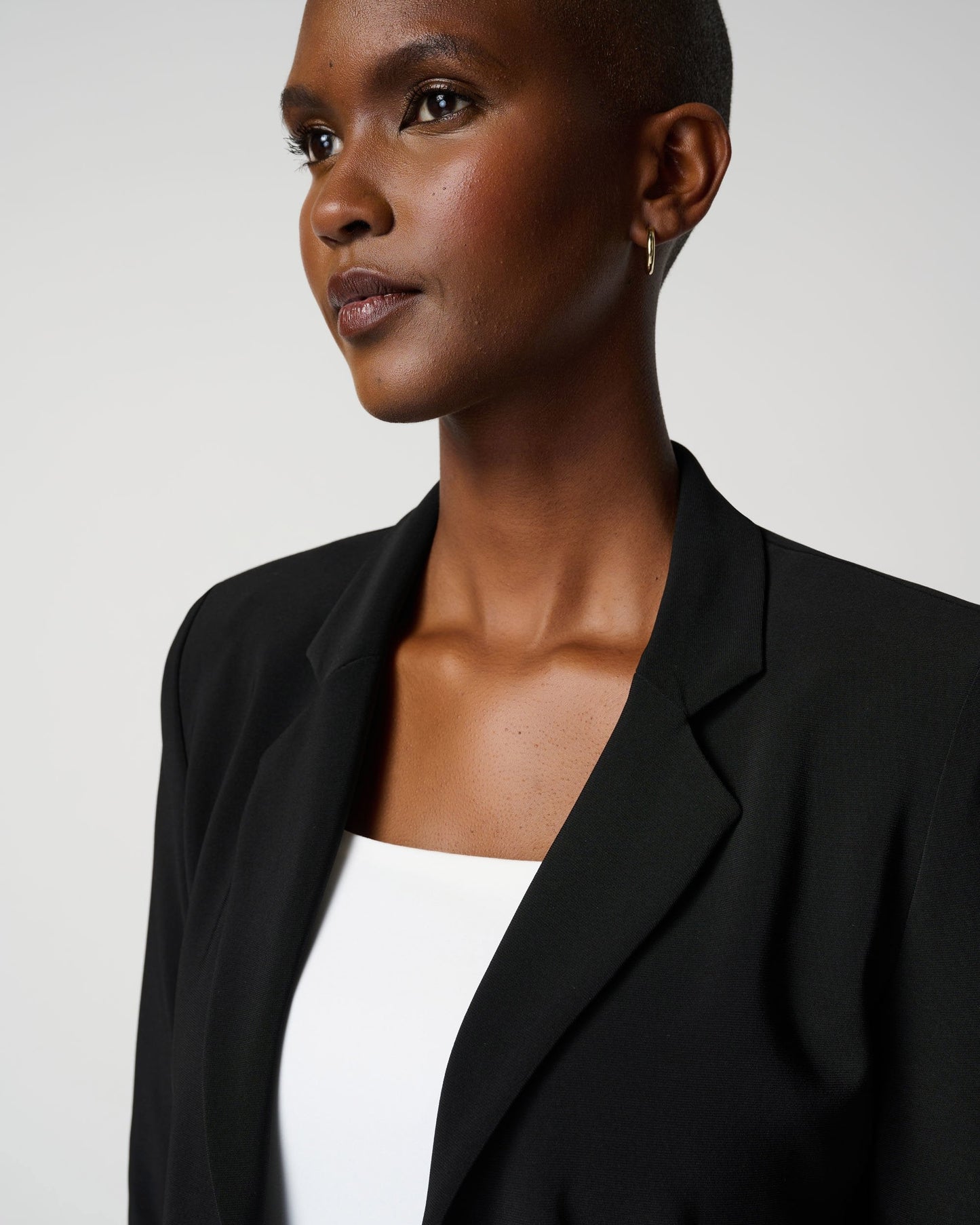 Woman wearing a black blazer over a white top against a plain background