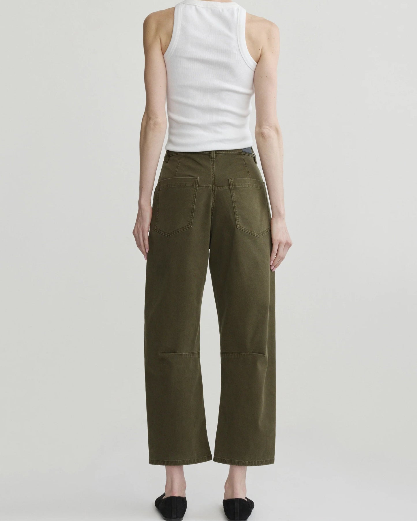 A model shown from the back wearing olive green wide-leg cropped pants, a white ribbed tank top, and black flats against a light gray studio background.