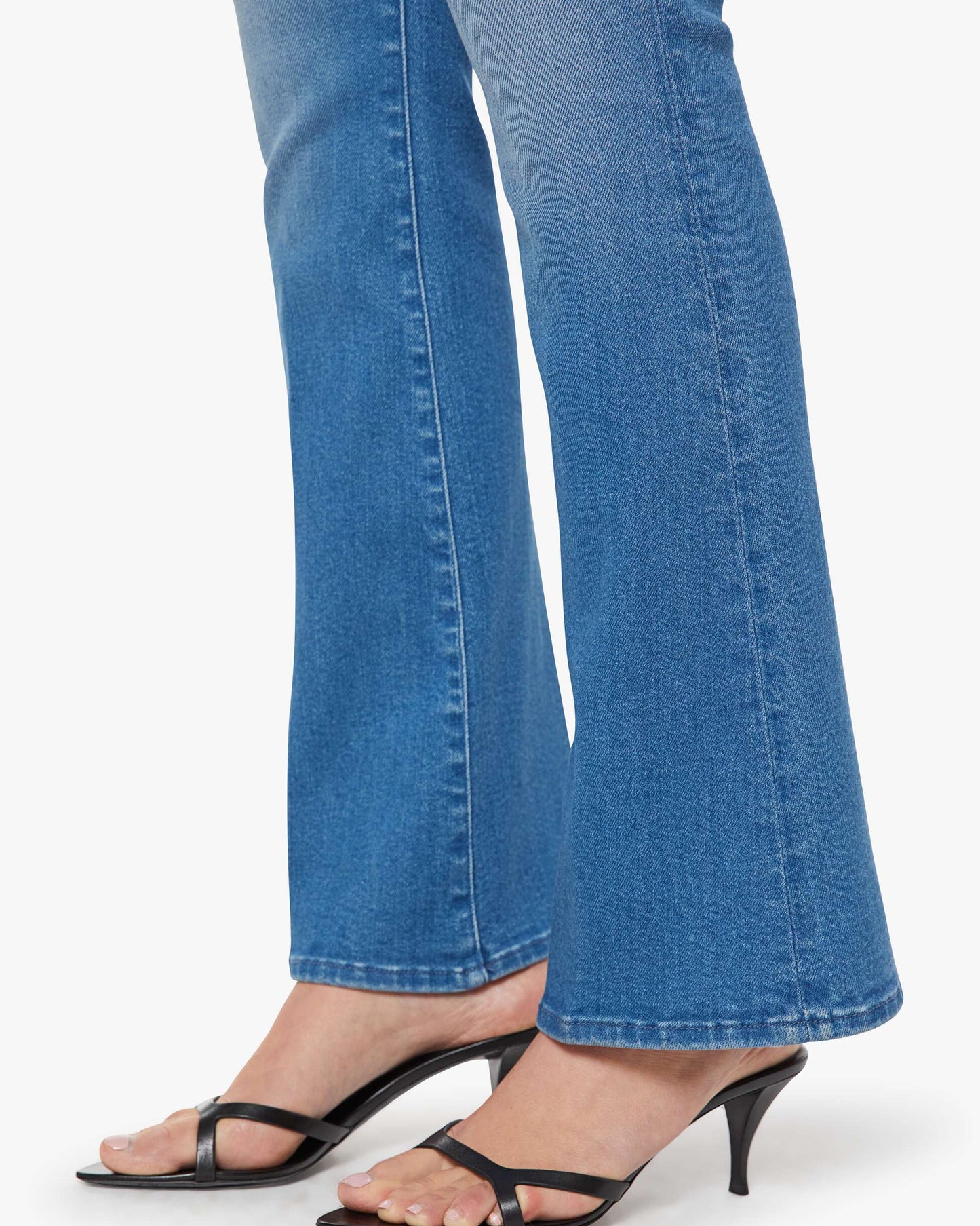 Blue jeans worn with black high-heeled sandals on a white background