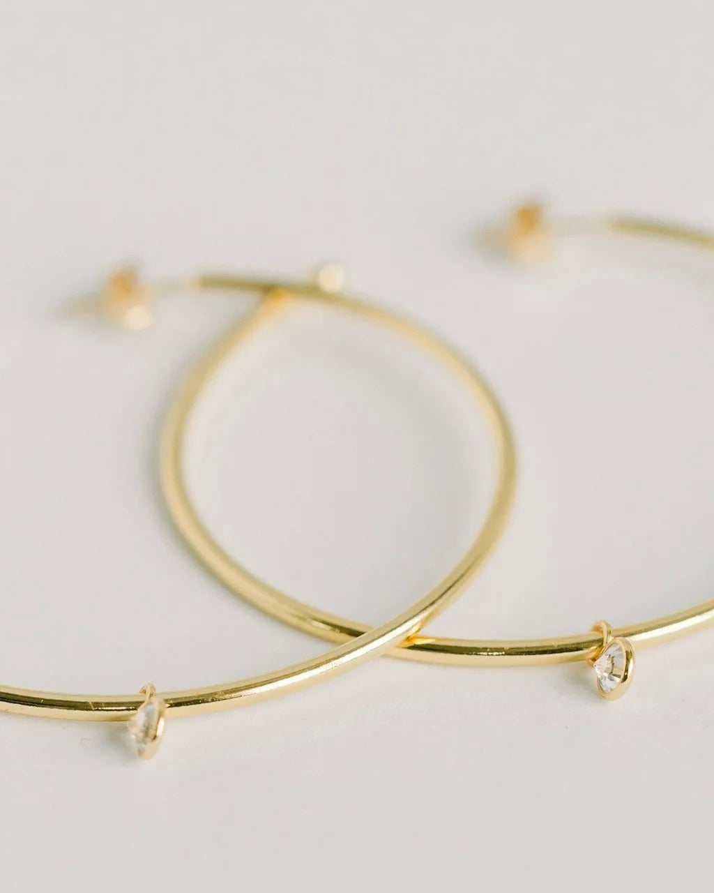 Close up photo of the Elli Parr Becca Gold Hoops laying flat against a white surface