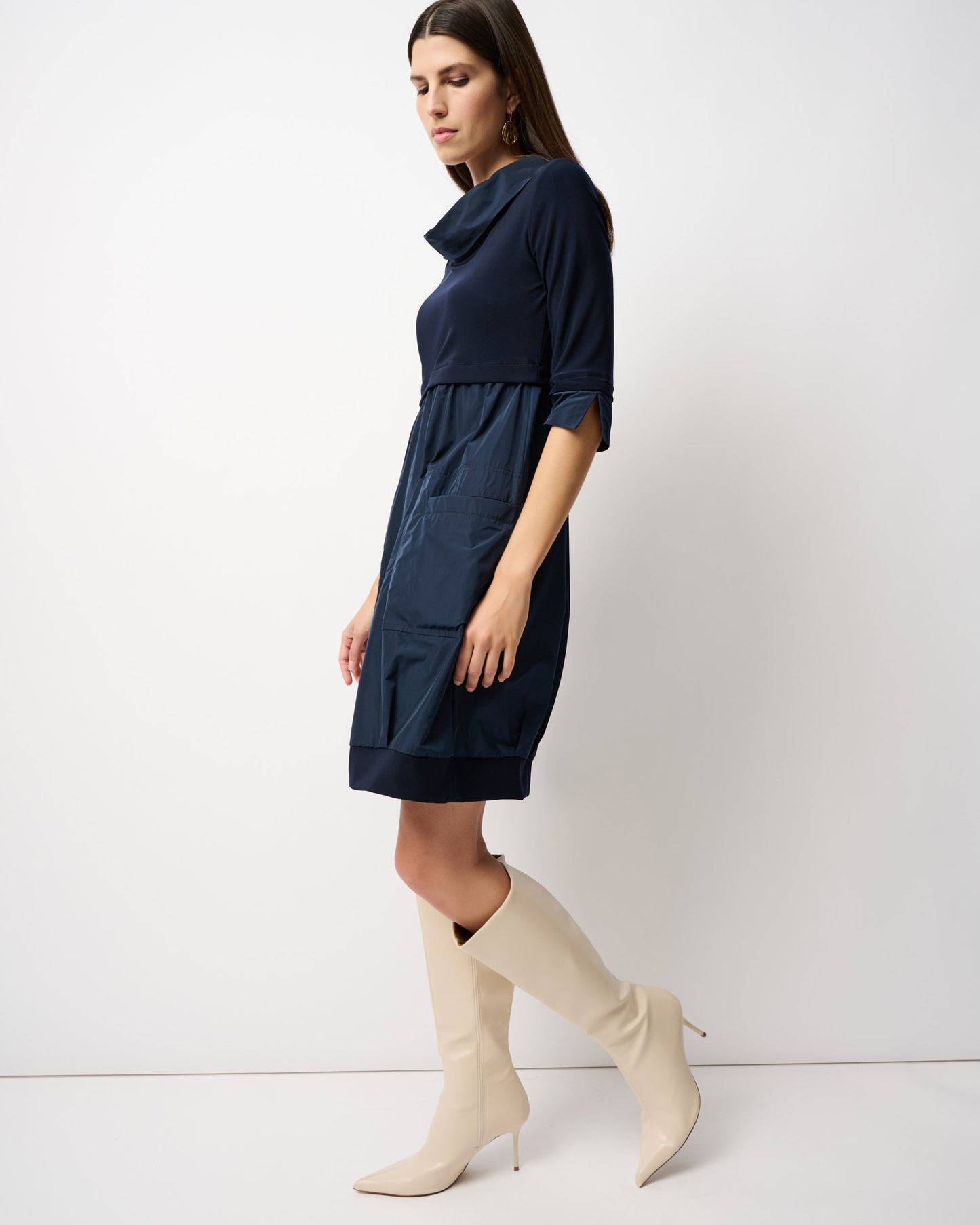 Woman wearing a navy dress and beige knee-high boots against a white background