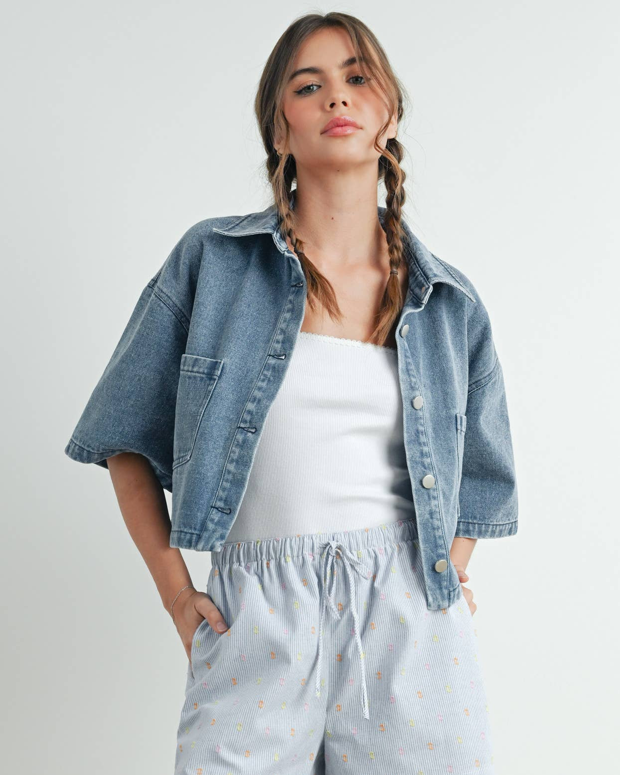 Woman wearing a denim jacket, white top, and light blue shorts on a plain background