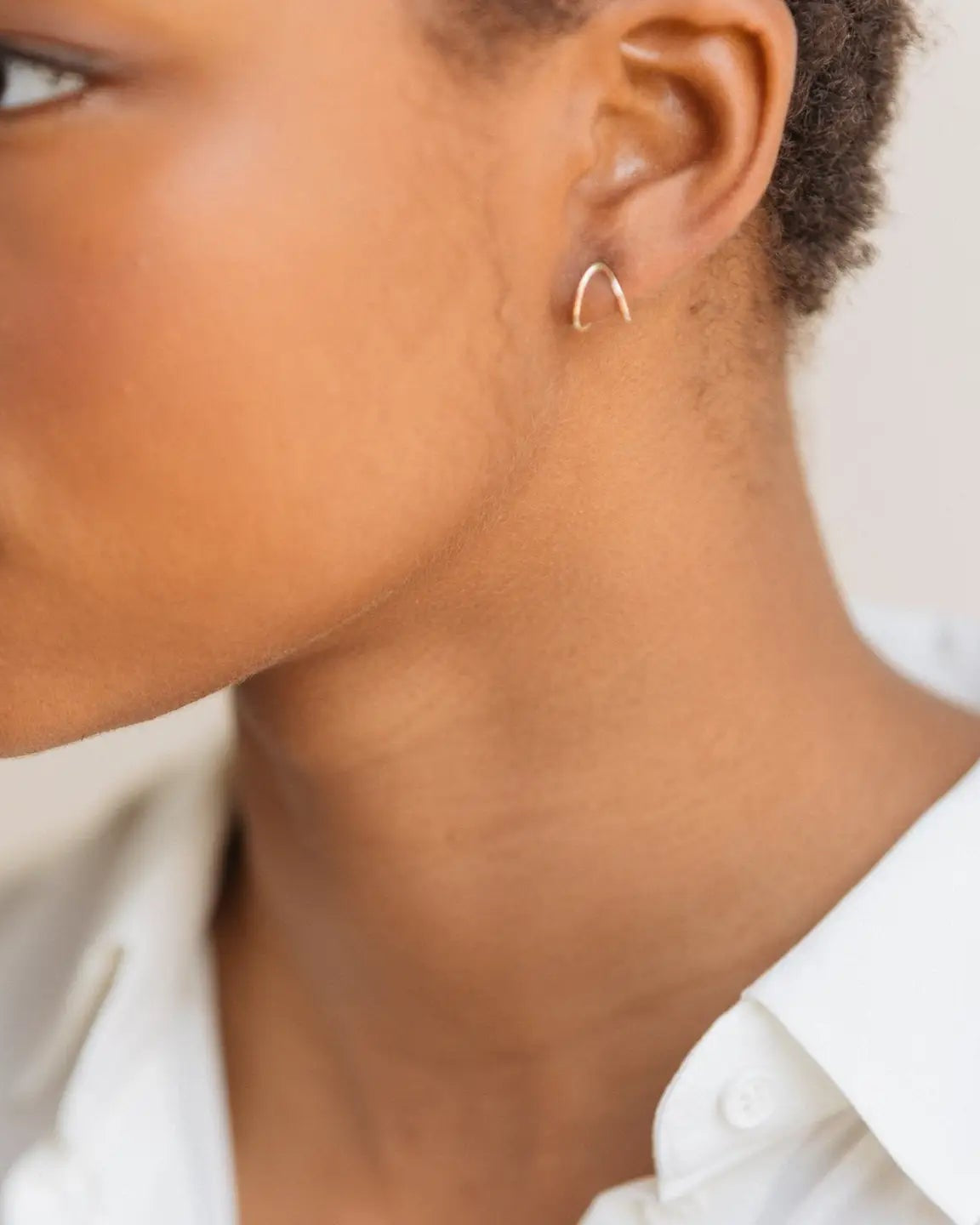 Close up of a model wearing the Able ear hug in gold with a white background.