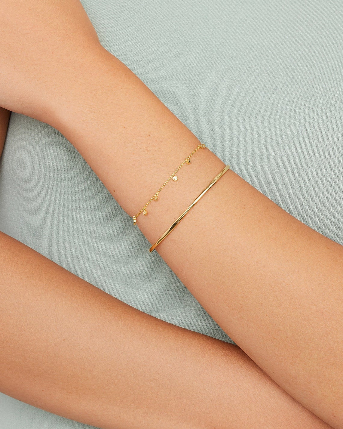 Delicate gold bracelet with small gold charms and thin gold band bracelet on models arm