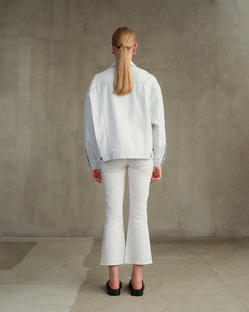 Person wearing a light-colored outfit standing against a plain wall.