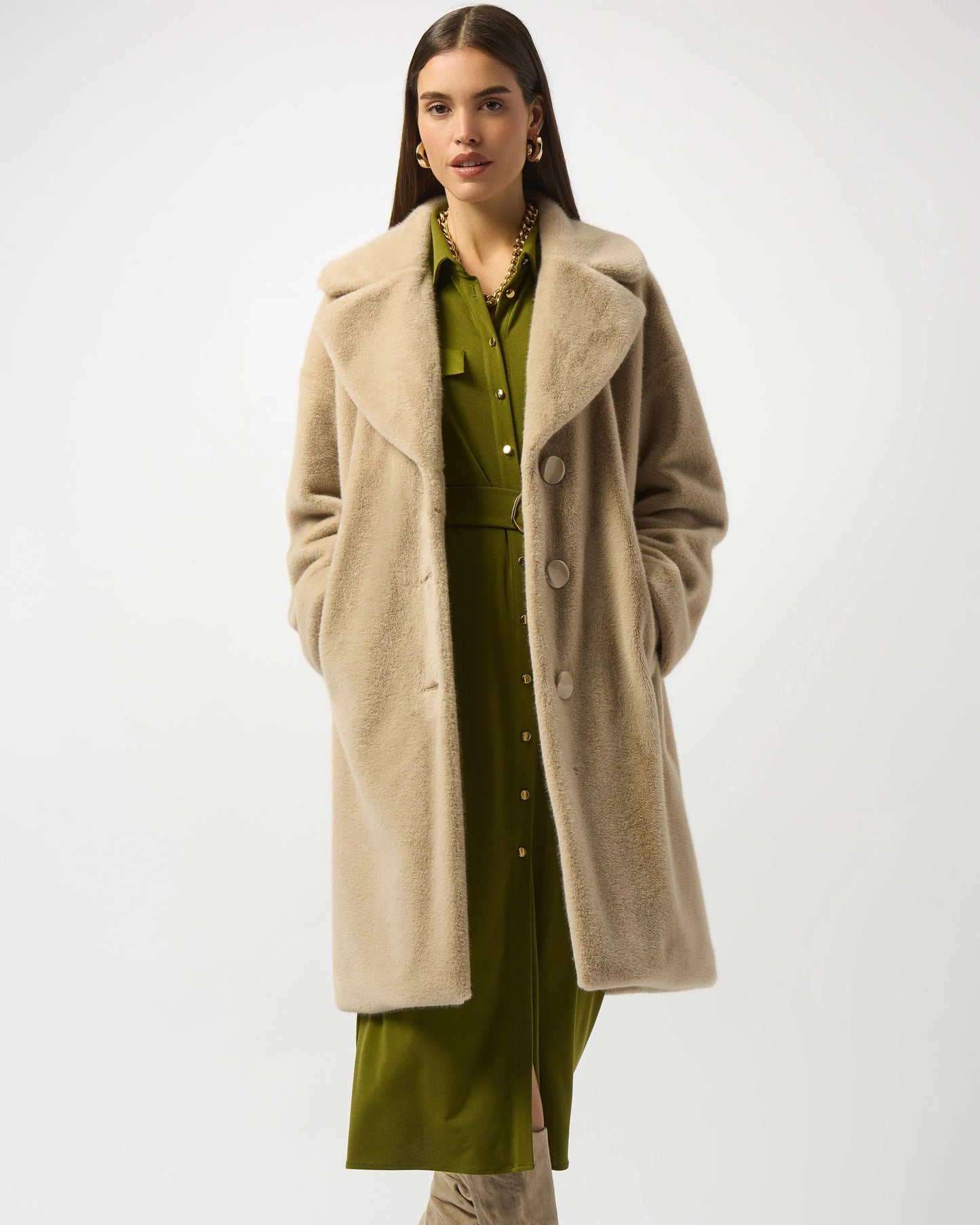 Woman wearing a beige coat over a green dress with beige knee-high boots on a white background