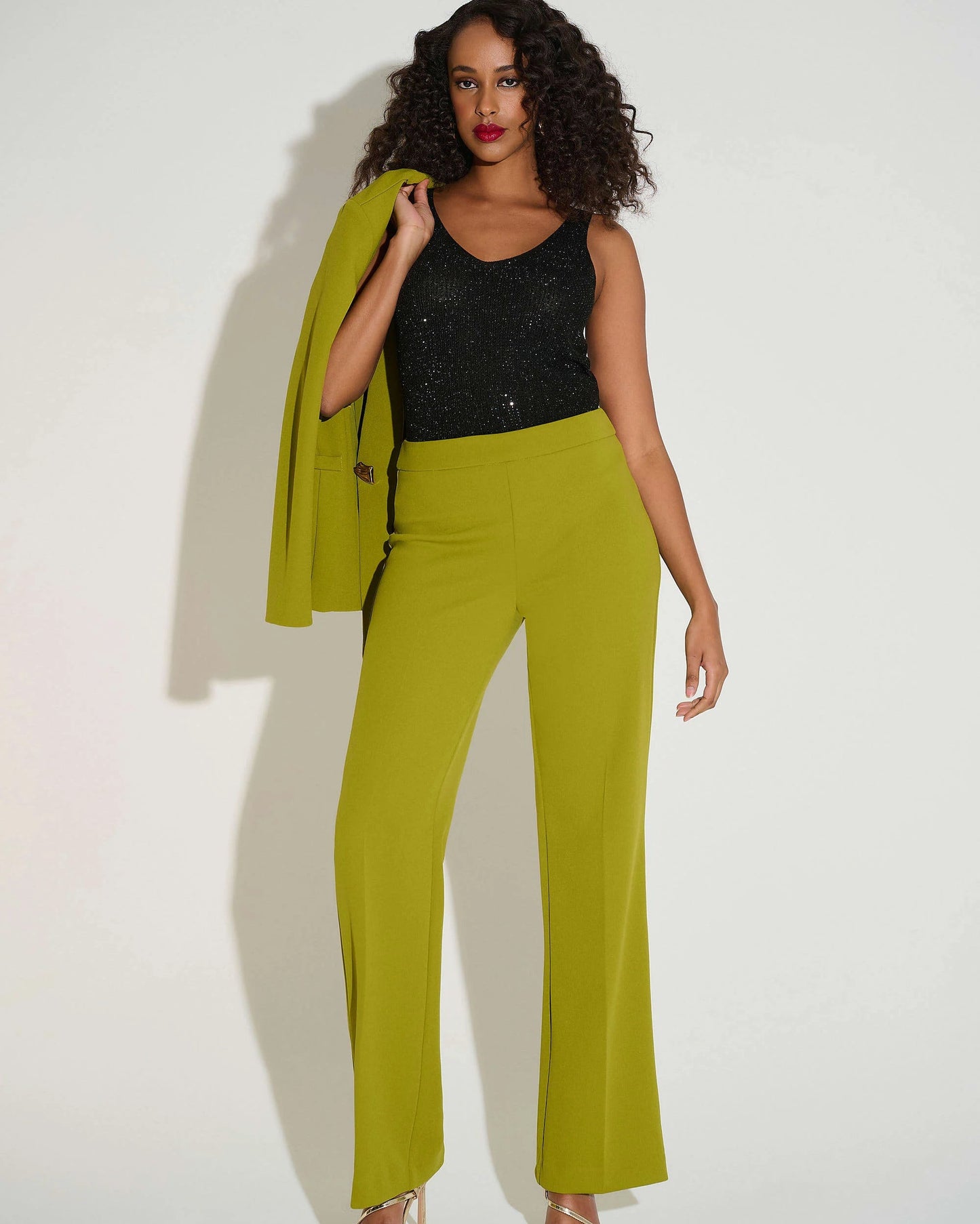 Woman wearing a black top and green pants with a green jacket on a white background