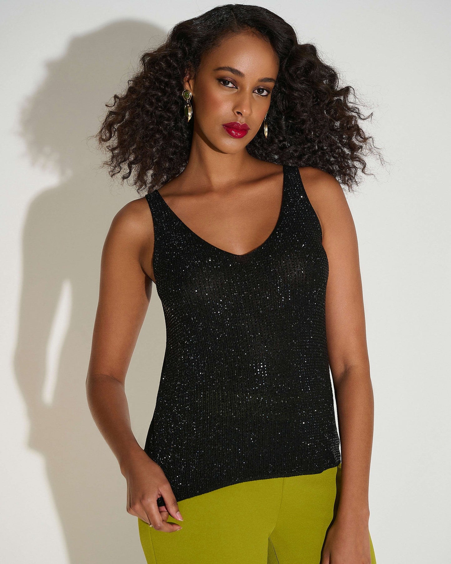 Woman wearing a black sleeveless top and green pants against a white background