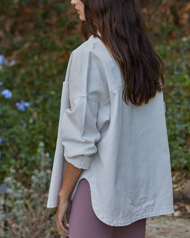Woman wearing a light gray oversized shirt outdoors with greenery in the background