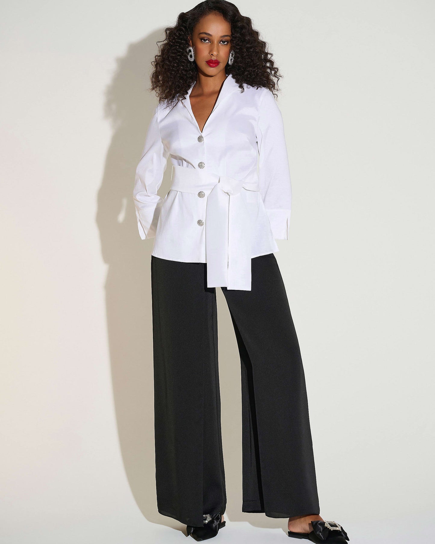 Woman wearing a white blazer and black pants against a white background