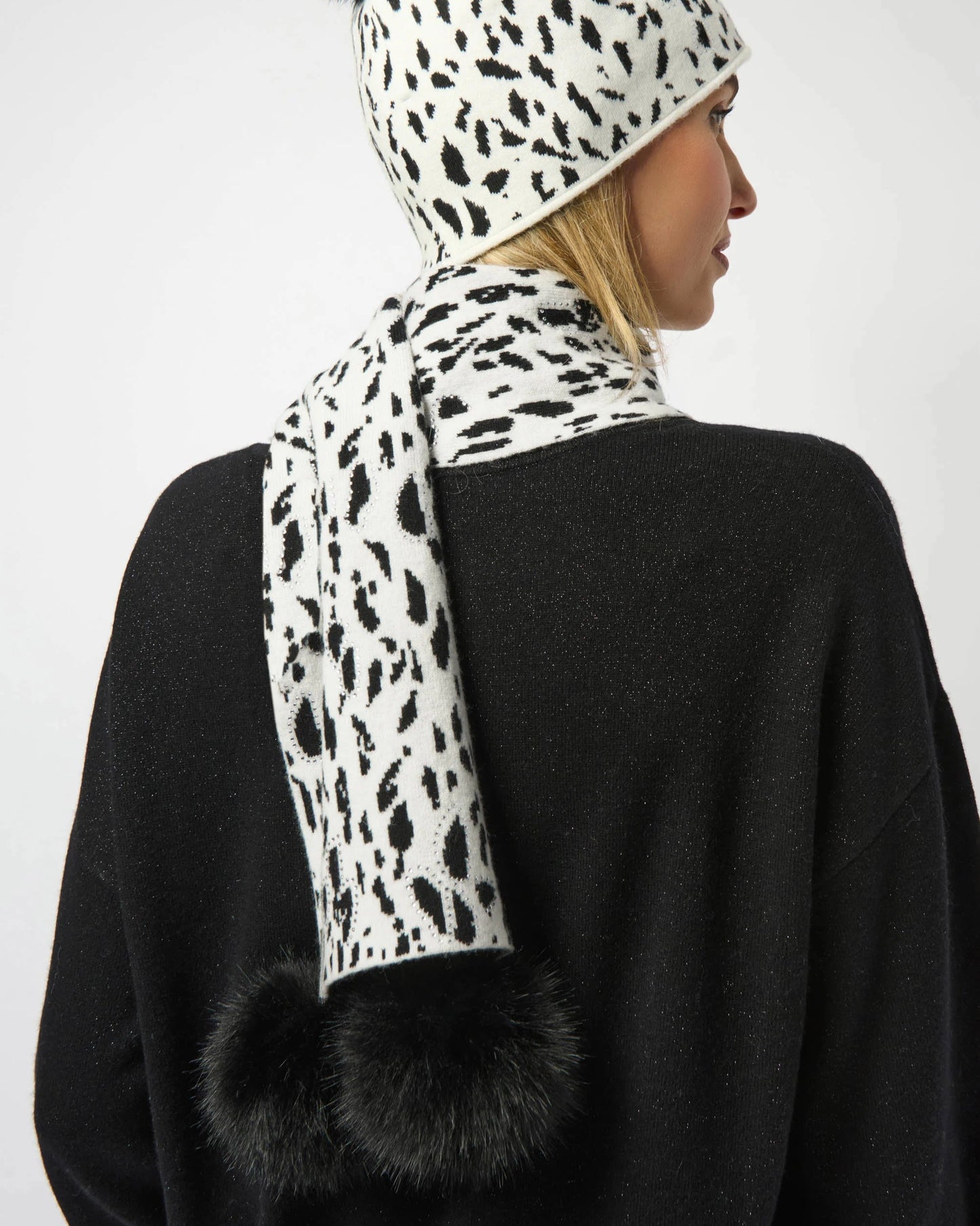 Person wearing a leopard print scarf with black pom-poms on a plain background