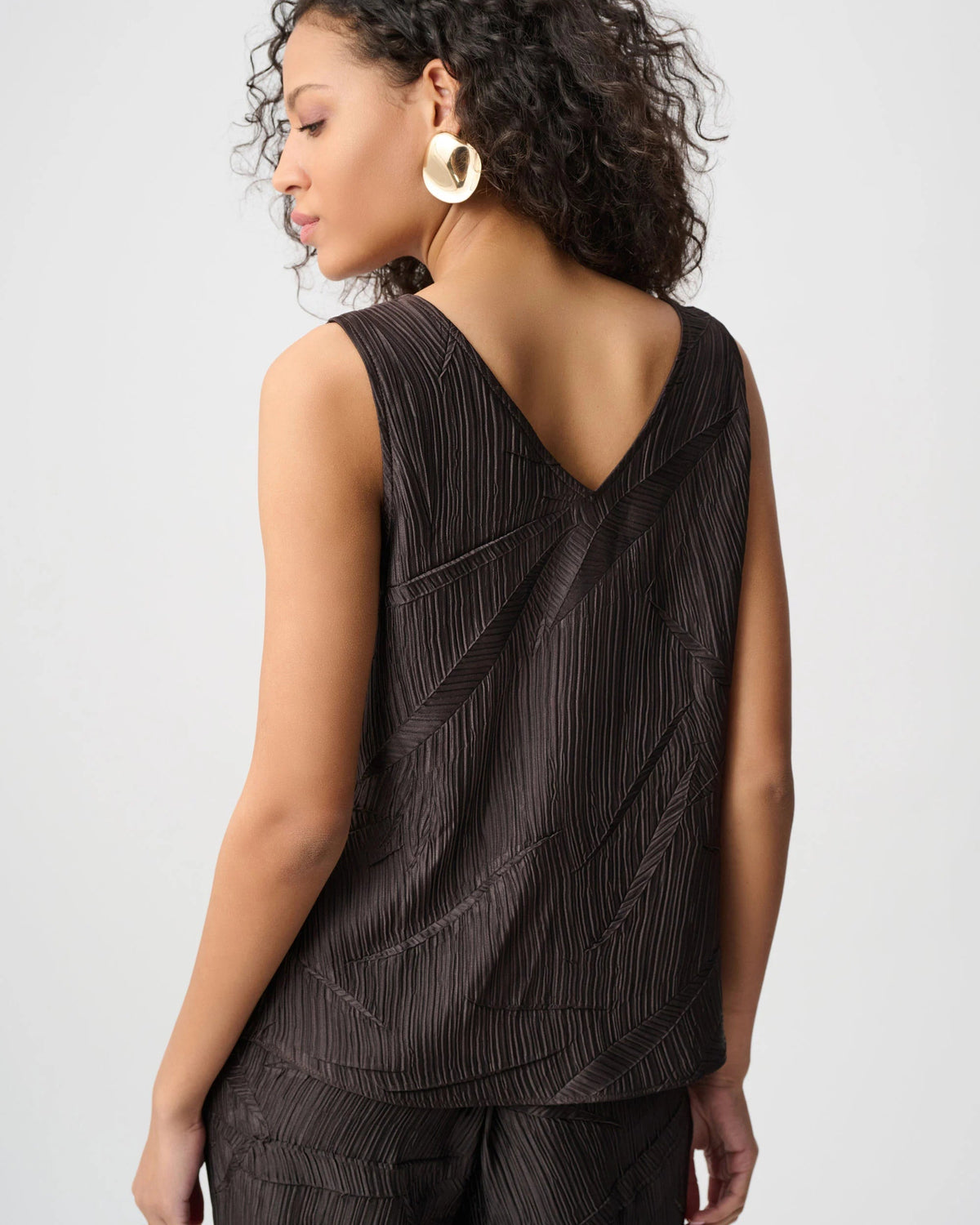 Woman wearing a black sleeveless top with a pleated design on a white background
