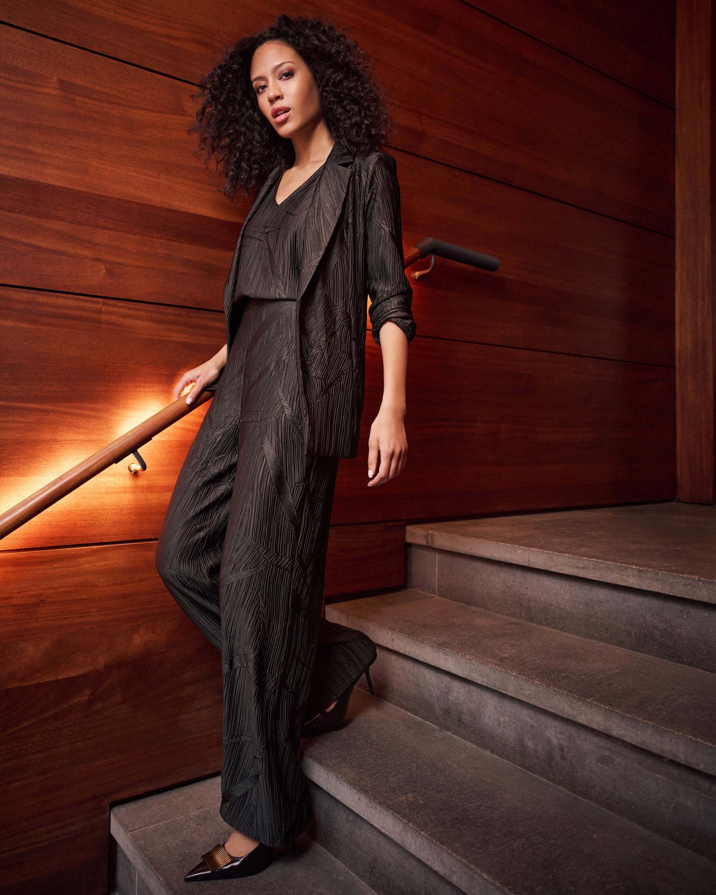 Woman in a dark outfit standing on a staircase with wooden walls.