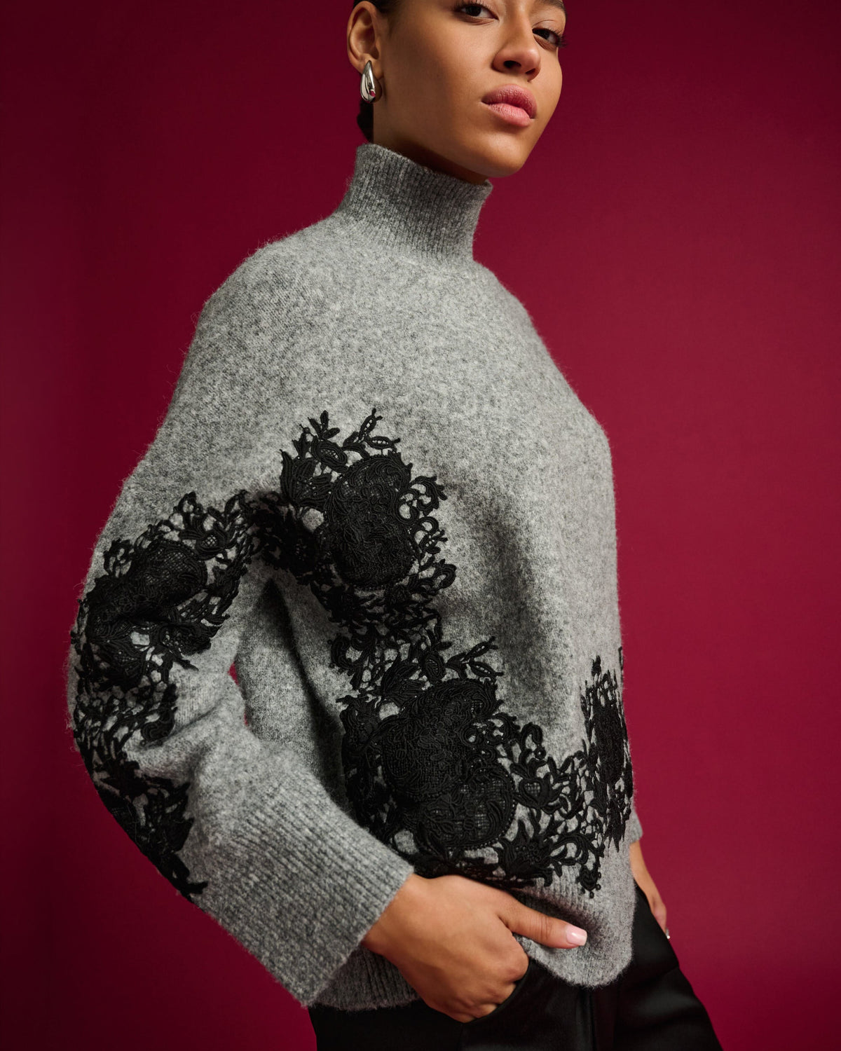 Woman wearing a gray sweater with black lace details against a red background