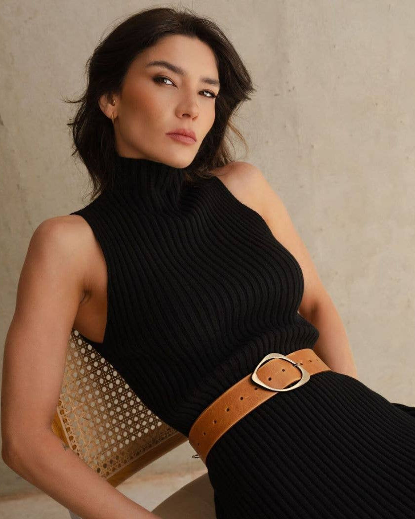 Woman wearing a black sleeveless top with a brown belt against a neutral background