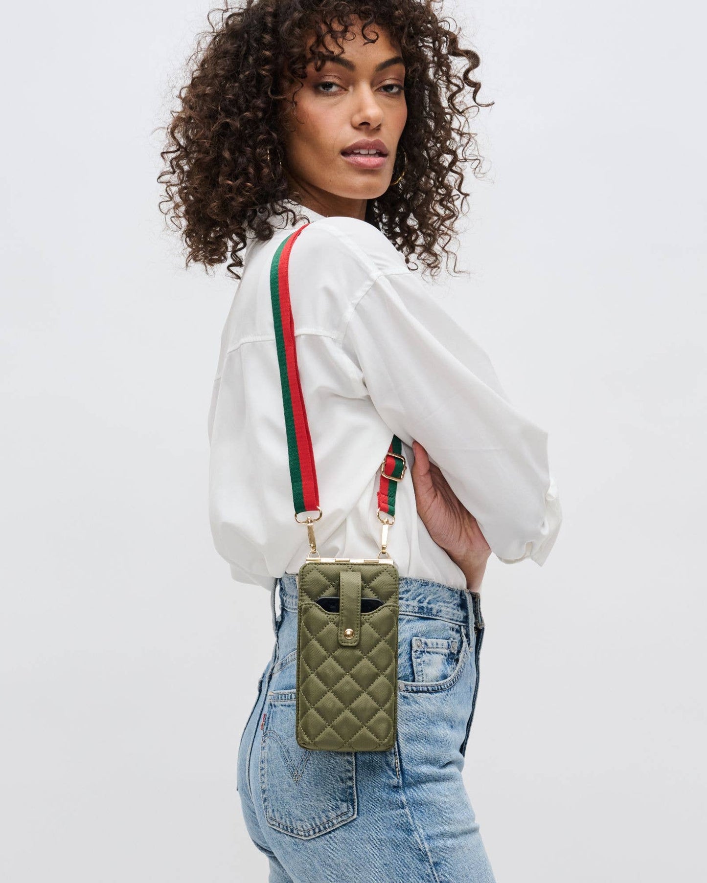 Woman wearing a white shirt, holding a green quilted bag with green and red straps.