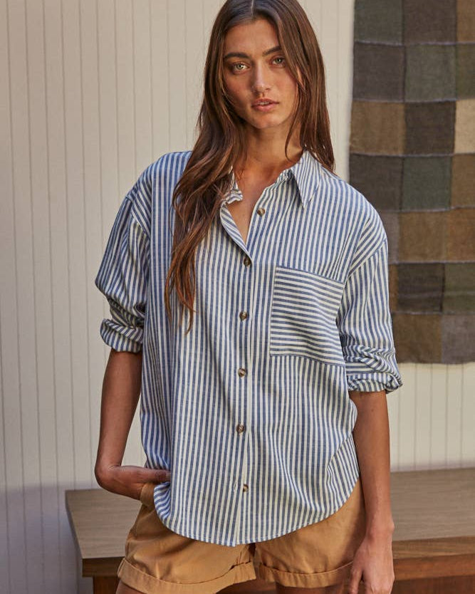 Front view of a woman wearing the By Together Woven Cotton Button Down in Blue against a decorated background