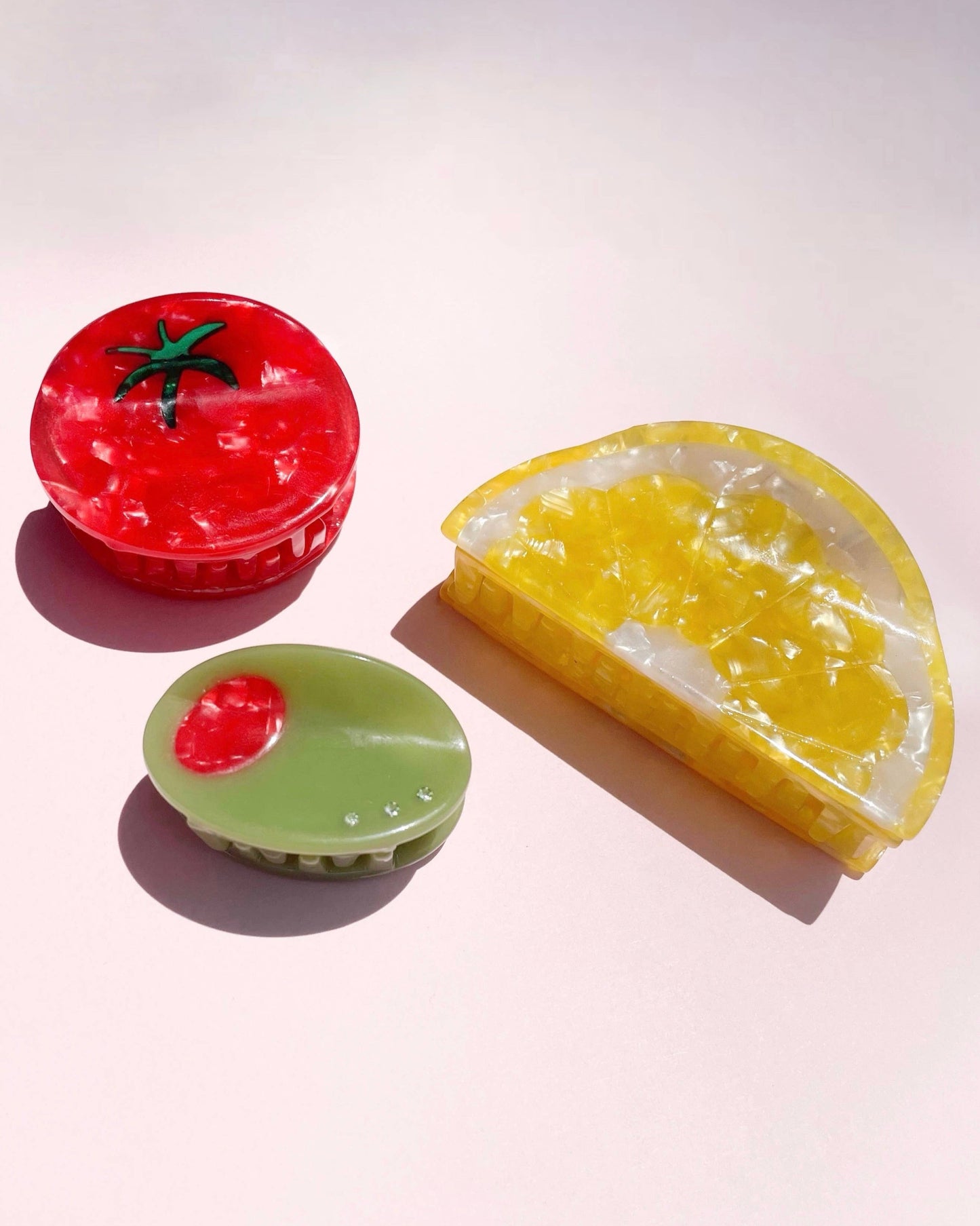 Three colorful food-shaped hair clips laying on a light pink background