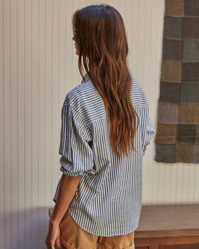 Back view of a woman wearing Front view of a woman wearing the By Together Woven Cotton Button Down in Blue against decorated background.