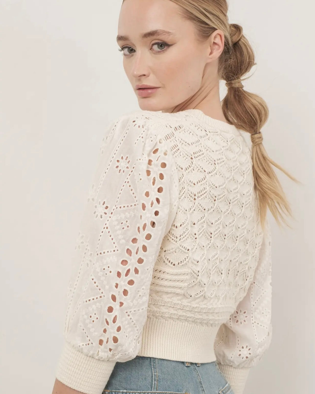 Side view of a model wearing the Hendry 3/4 sleeve cardigan in cream standing in front of a white background