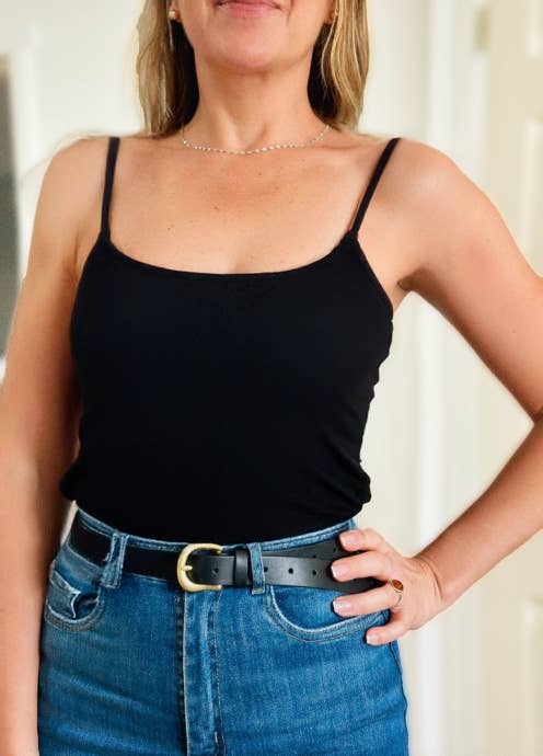 Woman wearing a black tank top and blue jeans with a blurred background