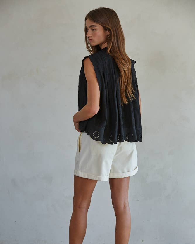 Woman wearing a black sleeveless top and white shorts against a plain background