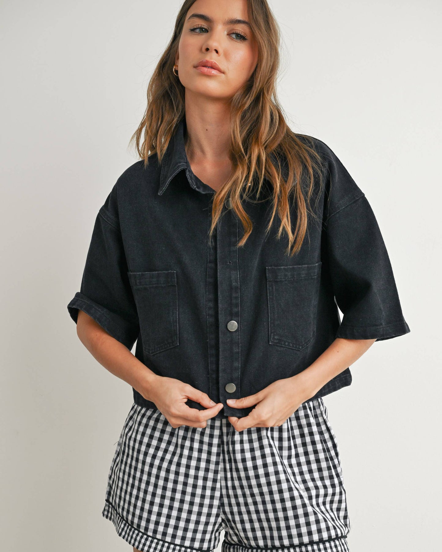 Woman wearing a black shirt and checkered shorts on a plain background