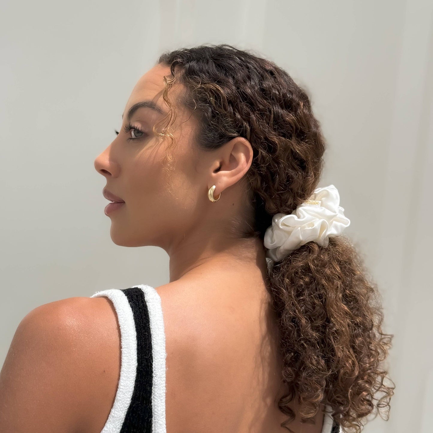 Woman with curly hair tied back wearing the HoneyLux Organic XL Silk Scrunchie in the color Bela against a neutral background
