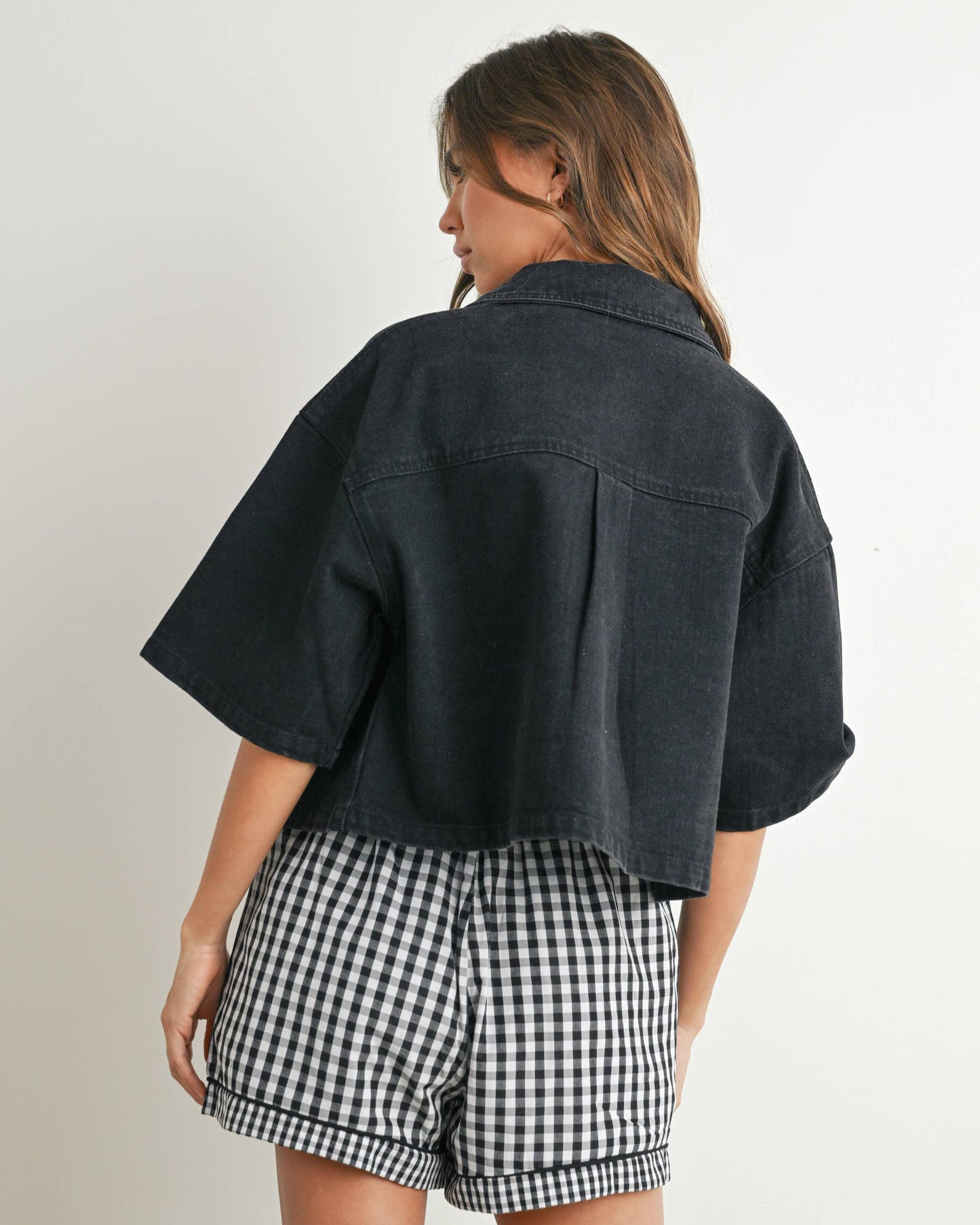 Person wearing a black jacket and checkered shorts on a plain background