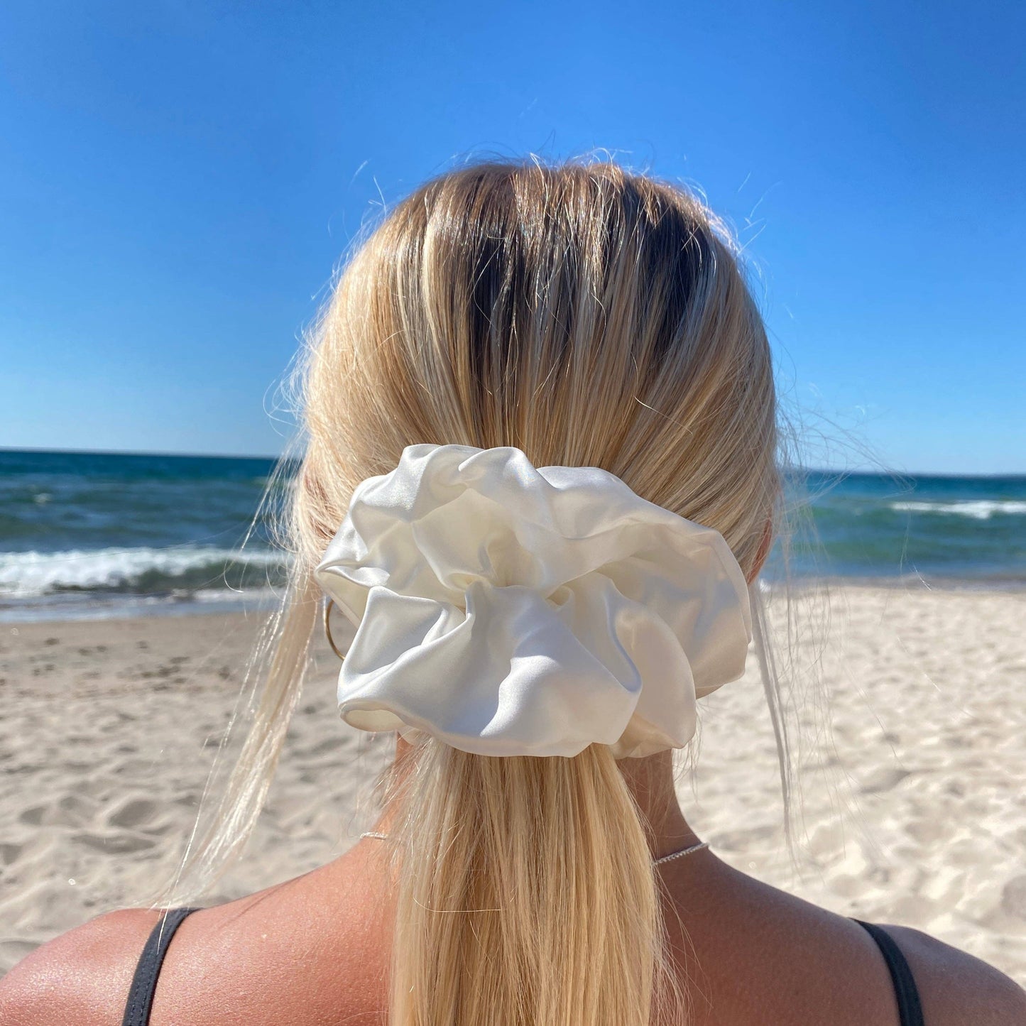 Back view of a woman wearing the HoneyLux Organic XL Silk Scrunchie in the color Bela in front of a blurred beach background