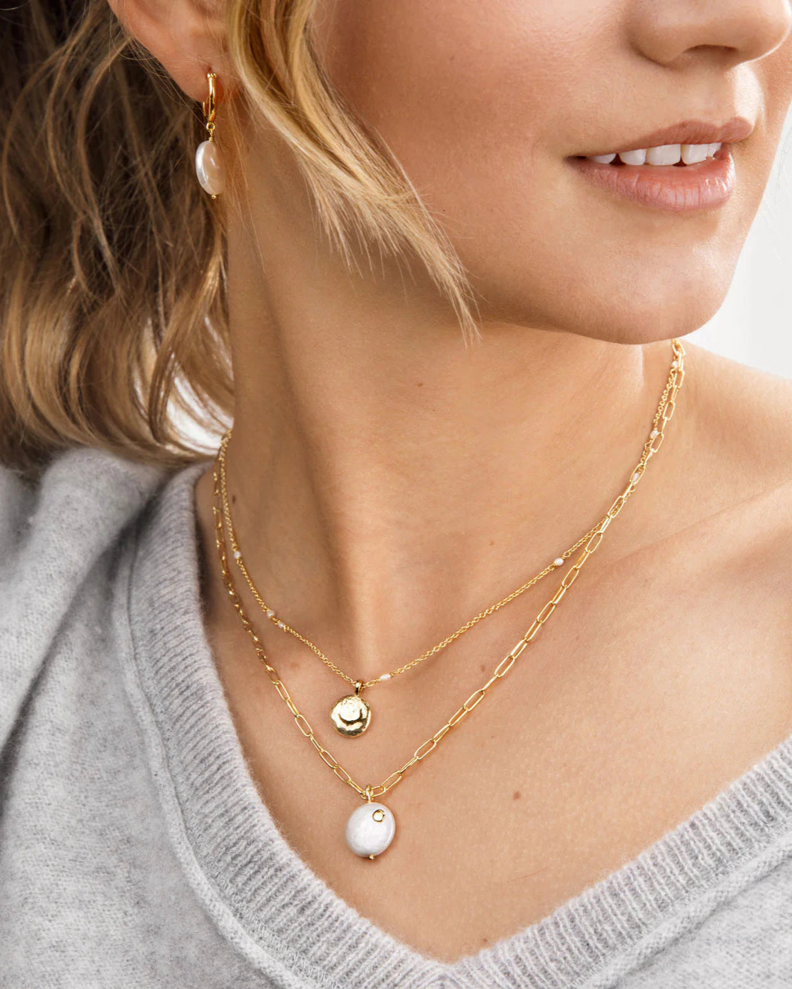Close up of the Gorjana Reese Pearl Necklace on a model wearing a grey sweater posing in front of a white background