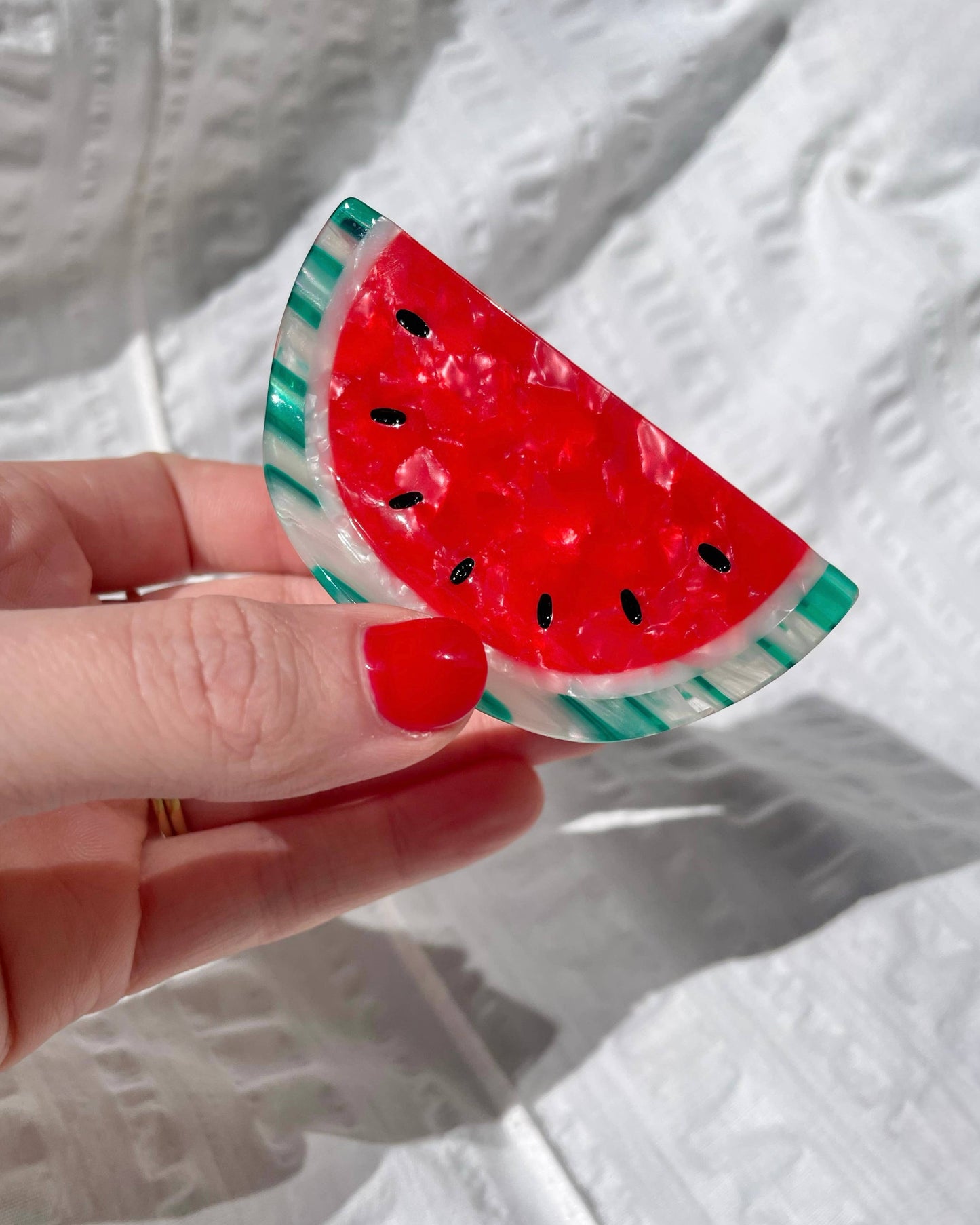 Hand holding a watermelon-shaped hairclip against a white background