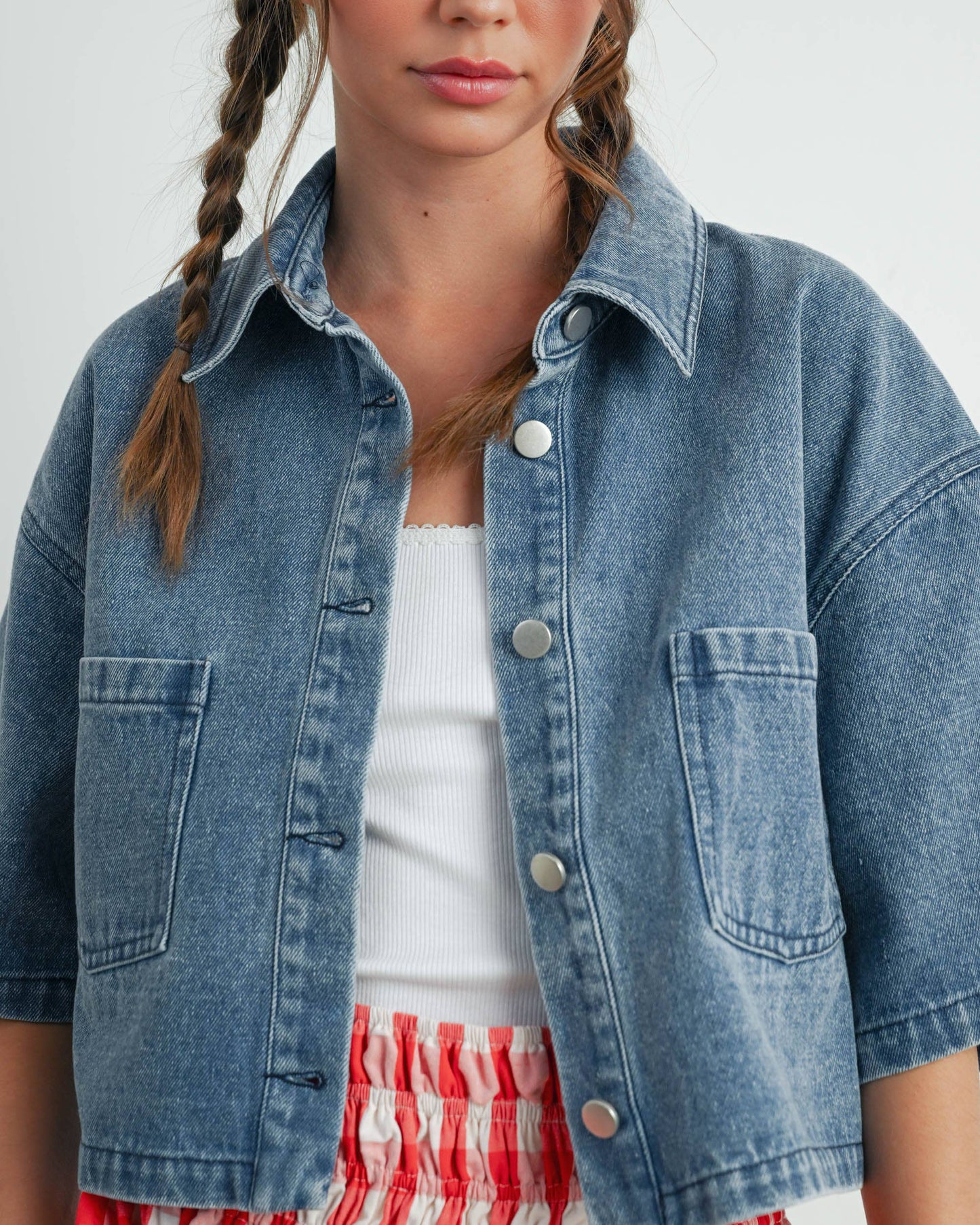Woman wearing a denim jacket over a white top and red plaid skirt on a plain background