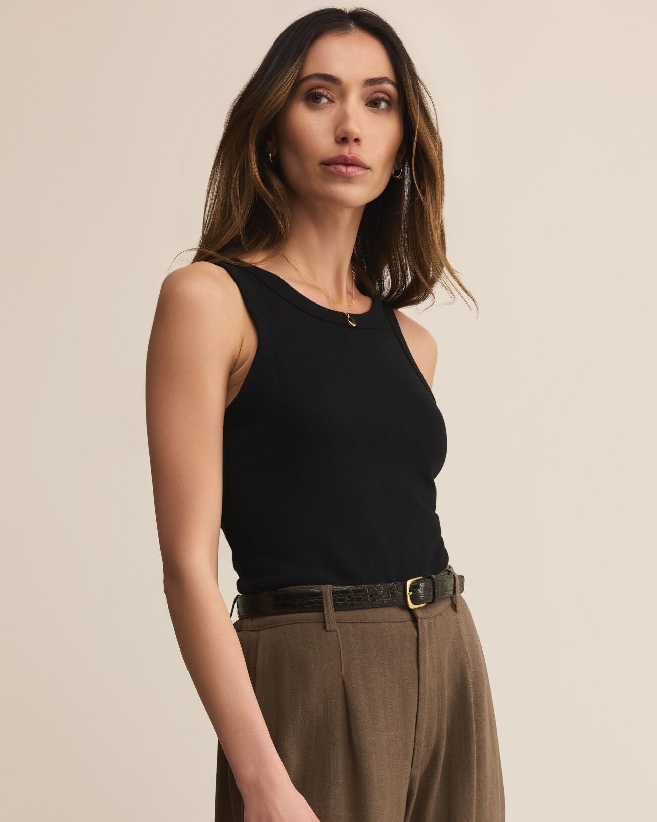 Woman wearing a black sleeveless top and brown pants against a beige background