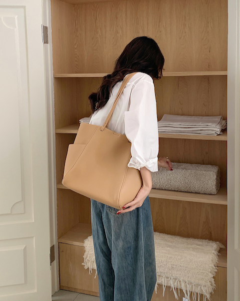 Person holding a beige tote bag in front of a wooden wardrobe.