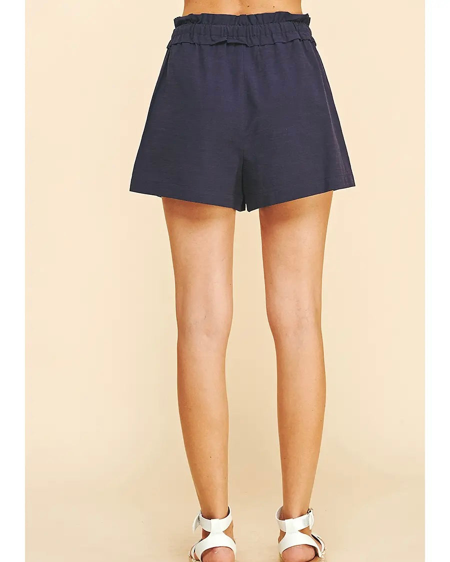 Model wearing Pinch Woven Shorts in navy on a brown background