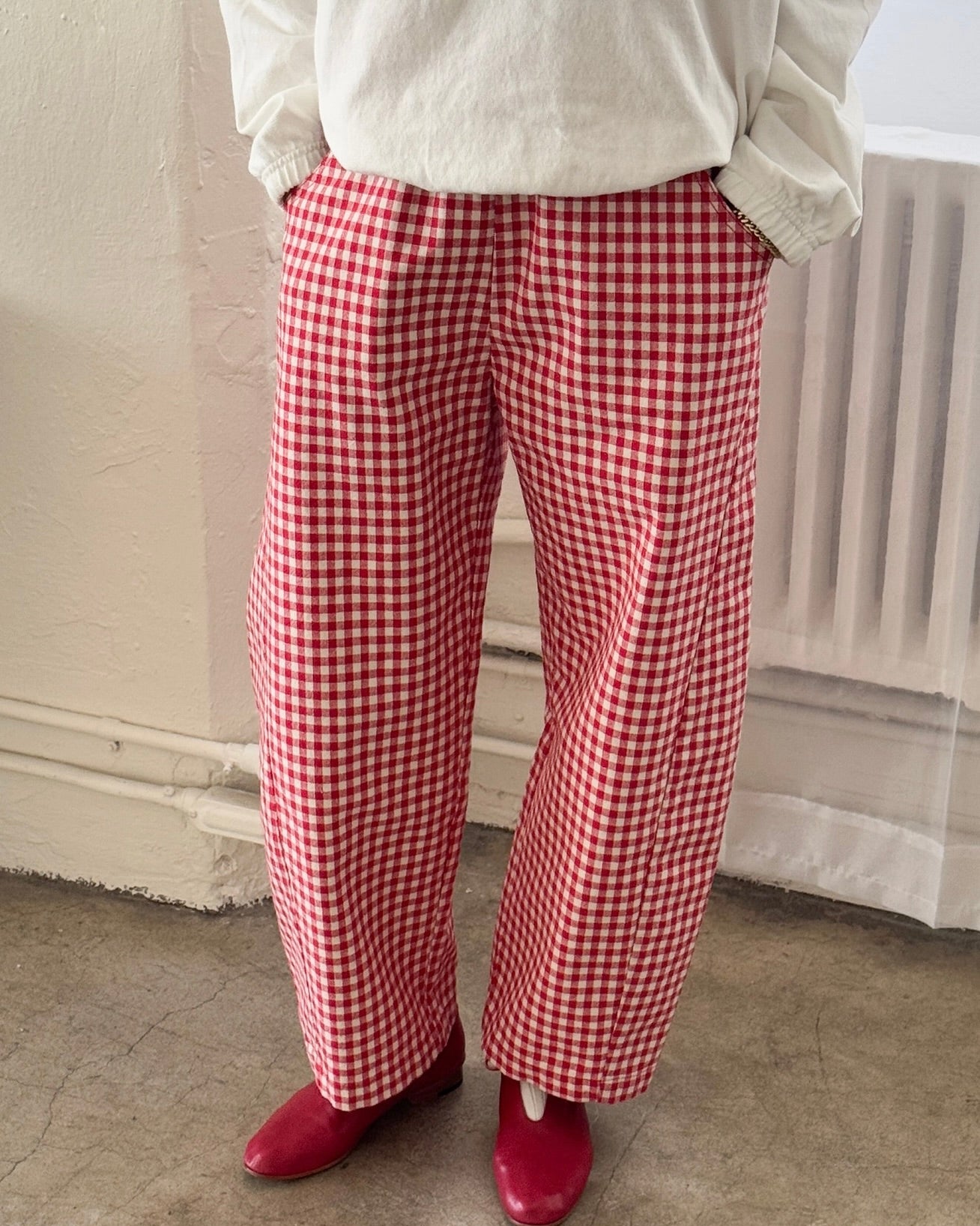 Front view of model wearing the Le Bon Shoppe arc pant in red gingham check standing in front of a white wall