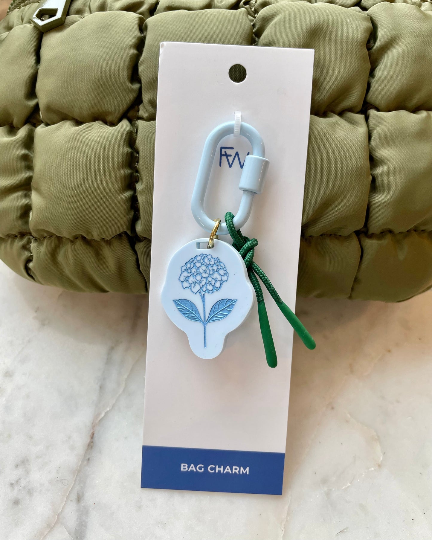 Freshwater curated goods Hydrangea Fish Carabiner Bag Charm in front of sol and selene quilted bag in army green on marble table
