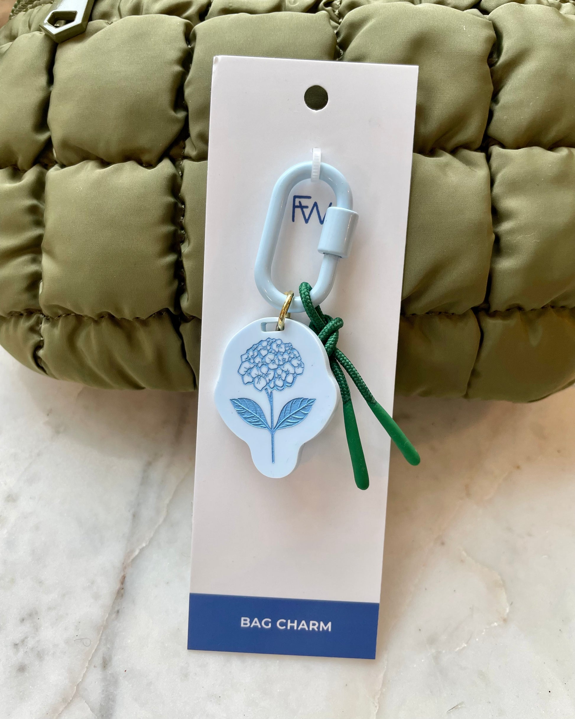 Freshwater curated goods Hydrangea Fish Carabiner Bag Charm in front of sol and selene quilted bag in army green on marble table