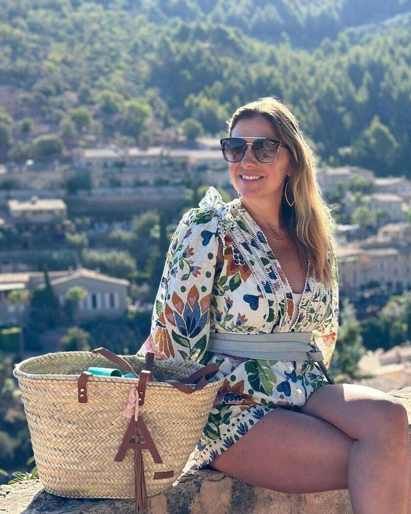 Woman in a floral dress sitting on a stone wall with a scenic background