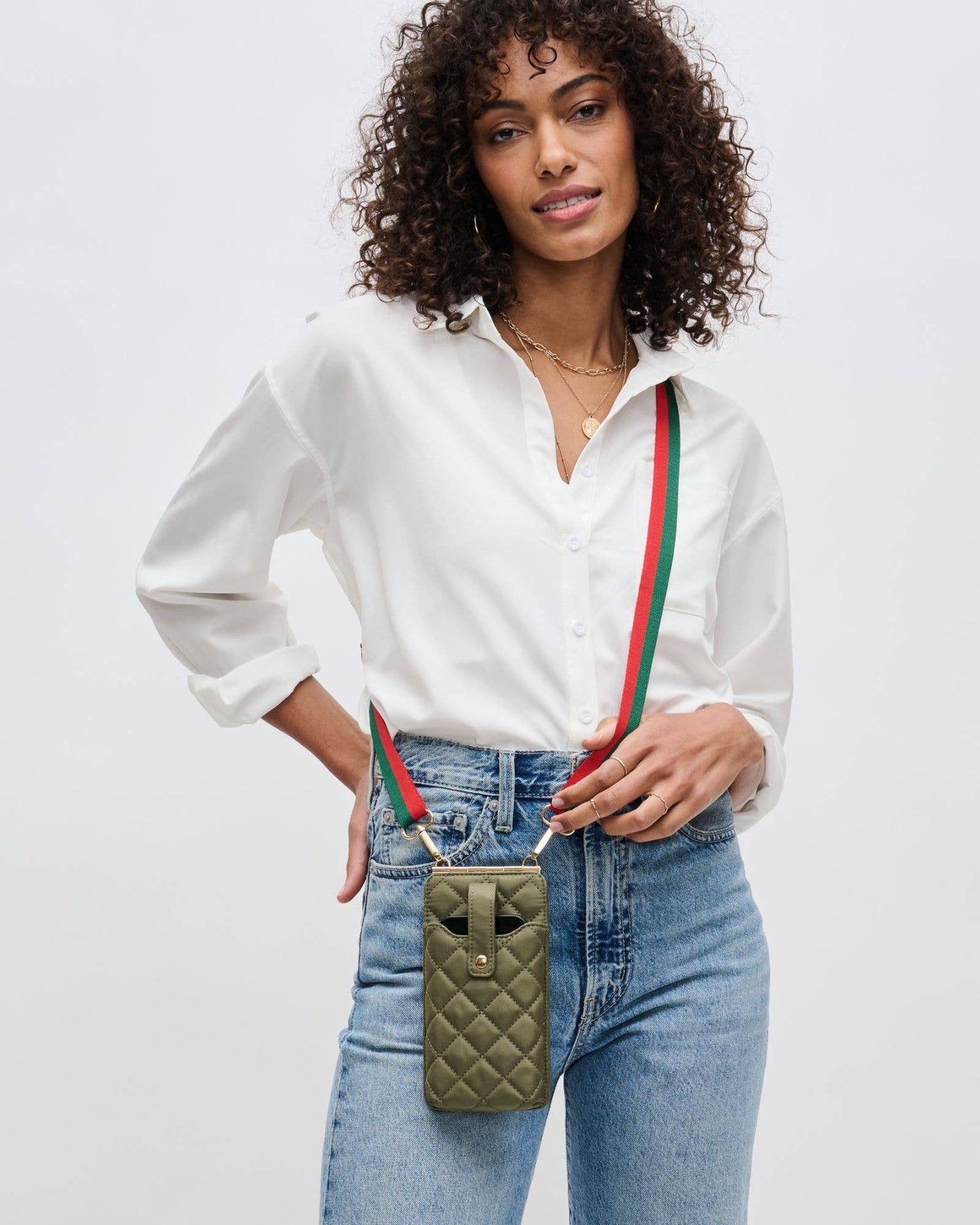 Woman wearing a white shirt and blue jeans with a green quilted bag featuring red and green straps.
