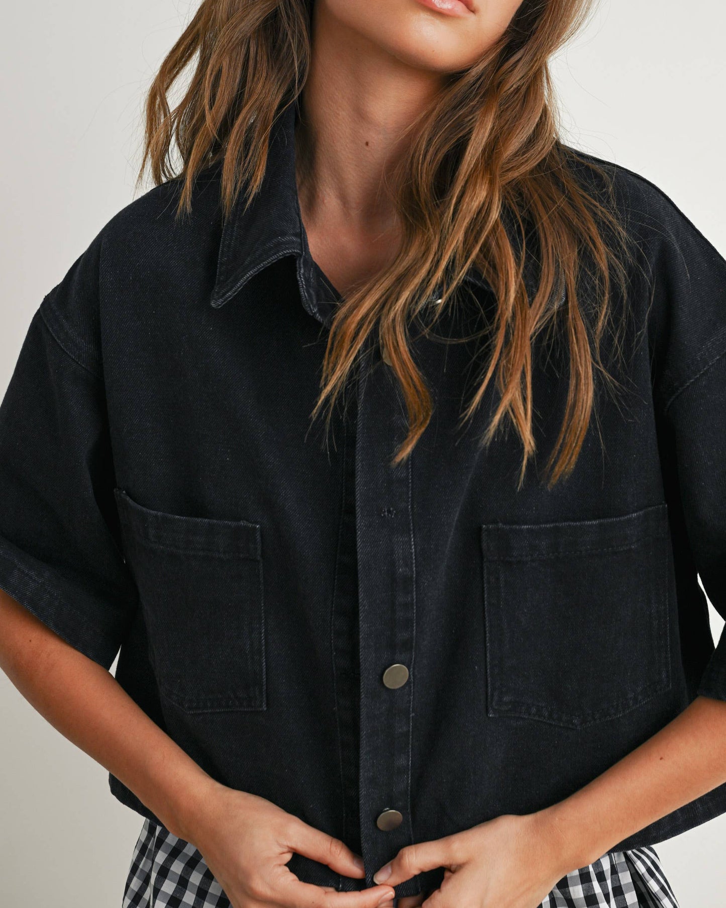 Woman wearing a black denim shirt against a plain background