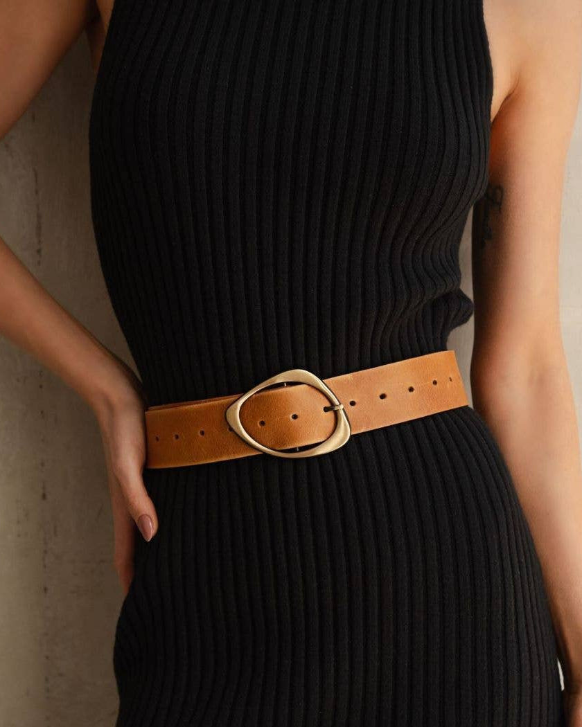 Person wearing a black dress with a brown belt against a neutral background