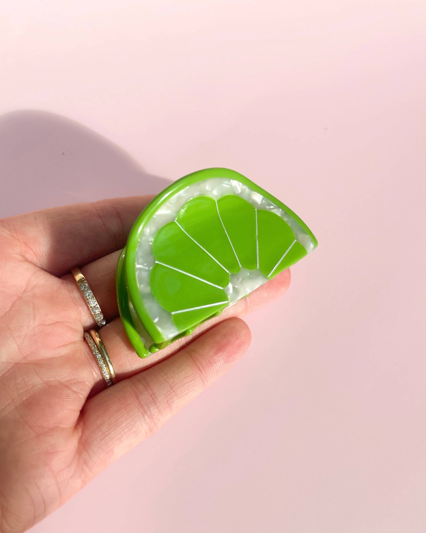 Hand holding a green lime slice hair clip against a pink background